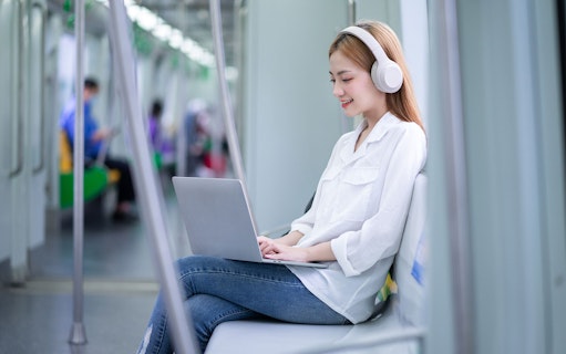 Woman using laptop with headphones on train, Japan Unlimited Pocket WiFi Rental.