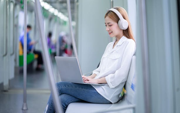 Woman using laptop with headphones on train, Japan Unlimited Pocket WiFi Rental.