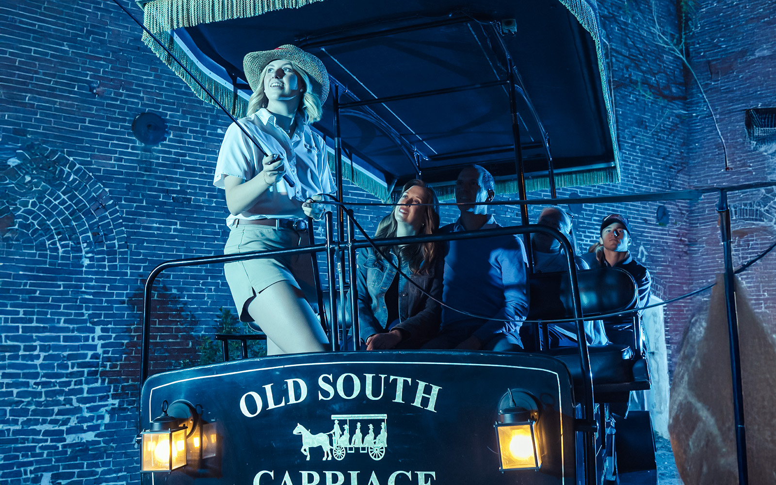 Charleston horse-drawn carriage tour guide with passengers at night.