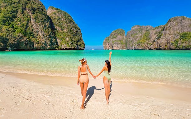Women walking on Maya Beach, Krabi, with limestone cliffs in the background.