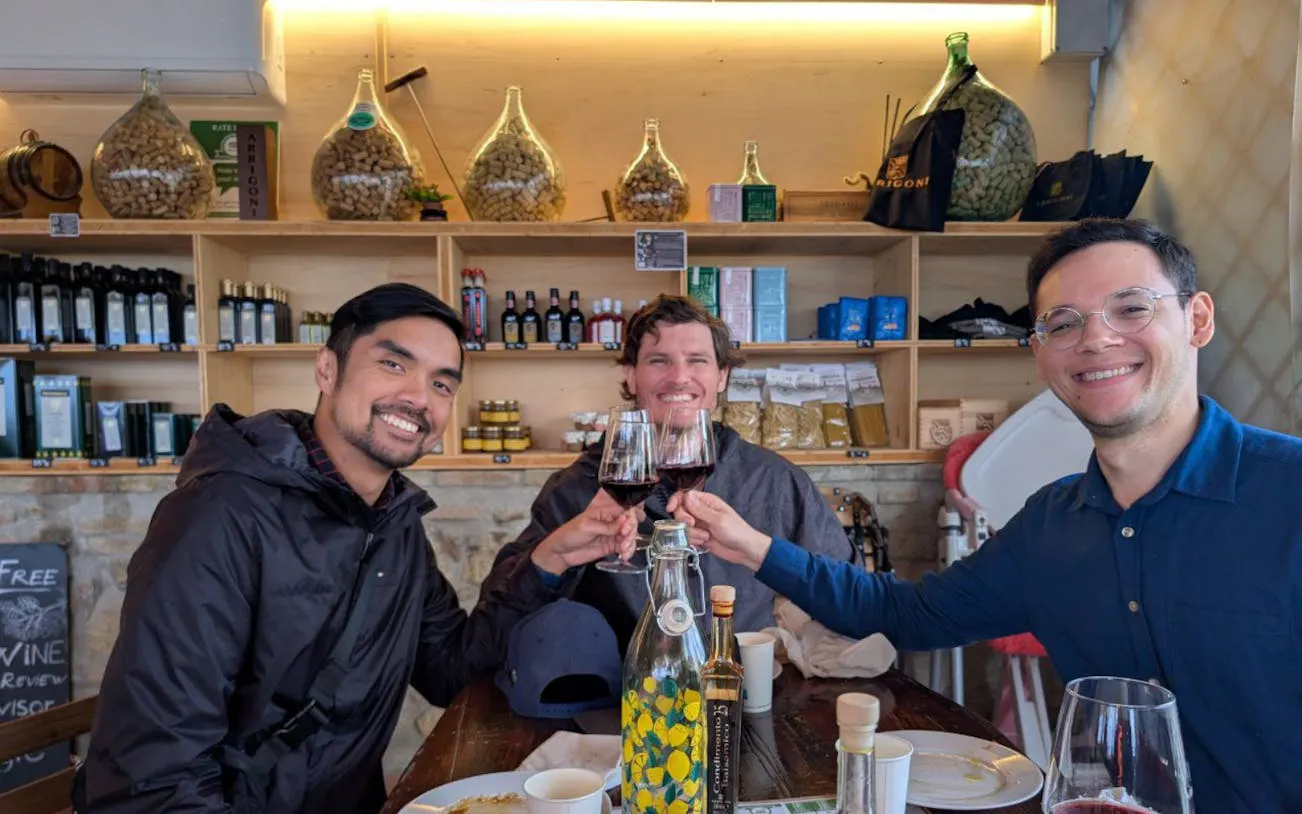 Three people toasting with red wine at a Tuscan winery tasting room.