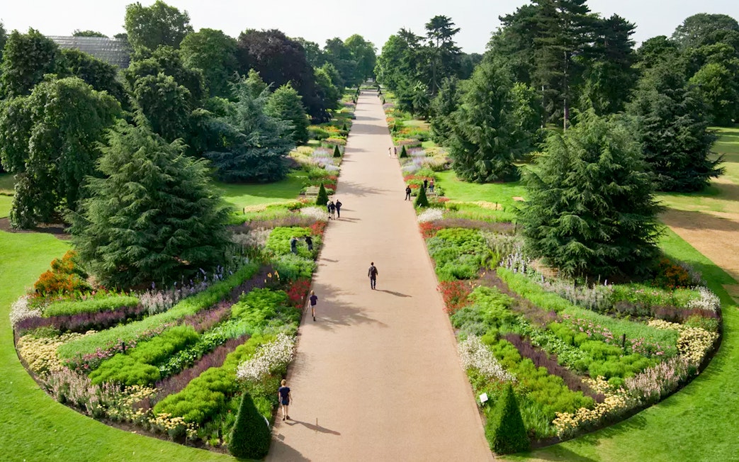 Pathway through vibrant gardens at Kew Gardens, London, with visitors strolling.