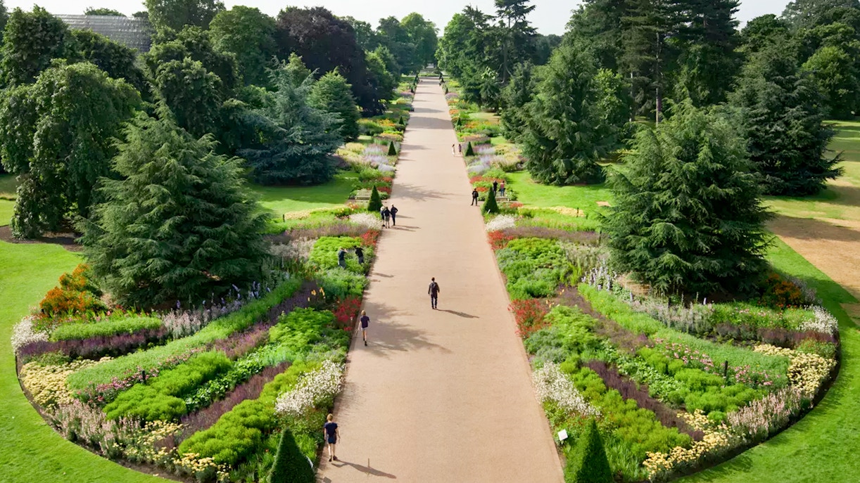 Pathway through vibrant gardens at Kew Gardens, London, with visitors strolling.