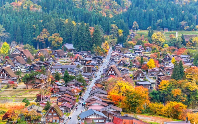 Traditional gassho-style houses in Shirakawa-go village surrounded by autumn foliage.