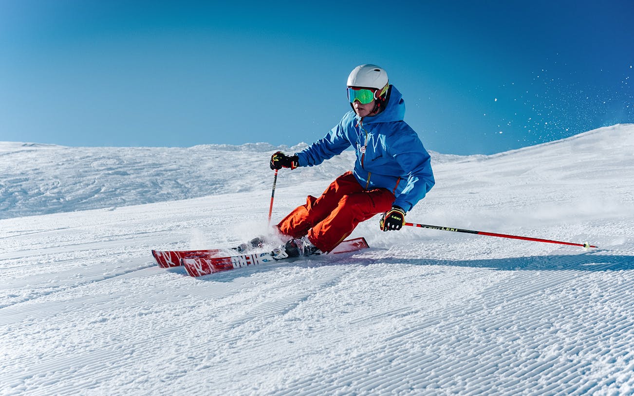 Skier in blue jacket and red pants on snowy slope with ski equipment.