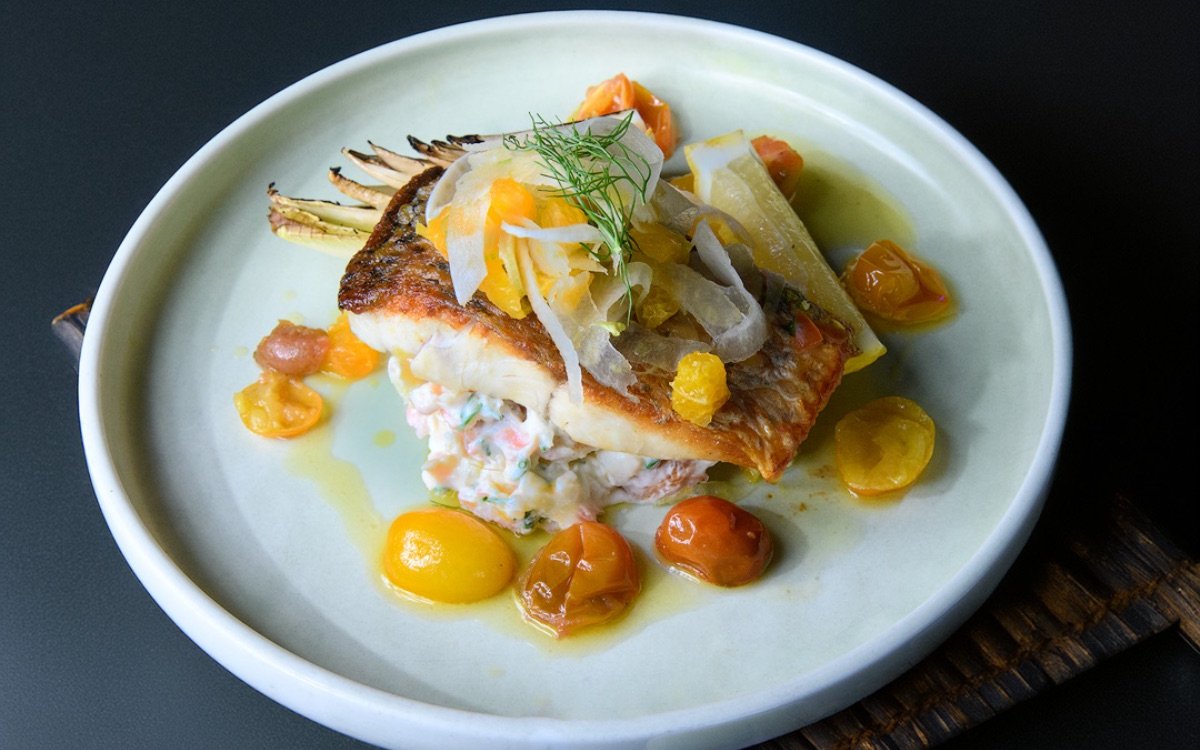Grilled fish with cherry tomatoes and garnish on a plate, served on Sydney Glass Boat Dinner Cruise.