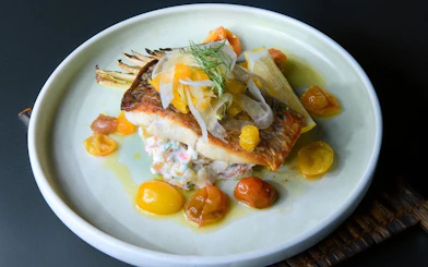 Grilled fish with cherry tomatoes and garnish on a plate, served on Sydney Glass Boat Dinner Cruise.