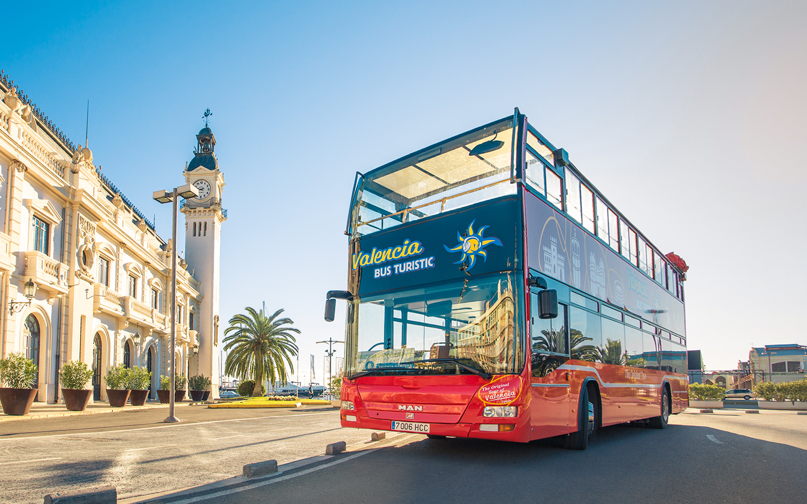 Valencia hop on hop off bus near historic clock tower and palm trees.