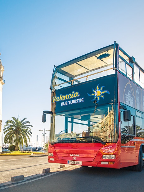 Valencia hop on hop off bus near historic clock tower and palm trees.