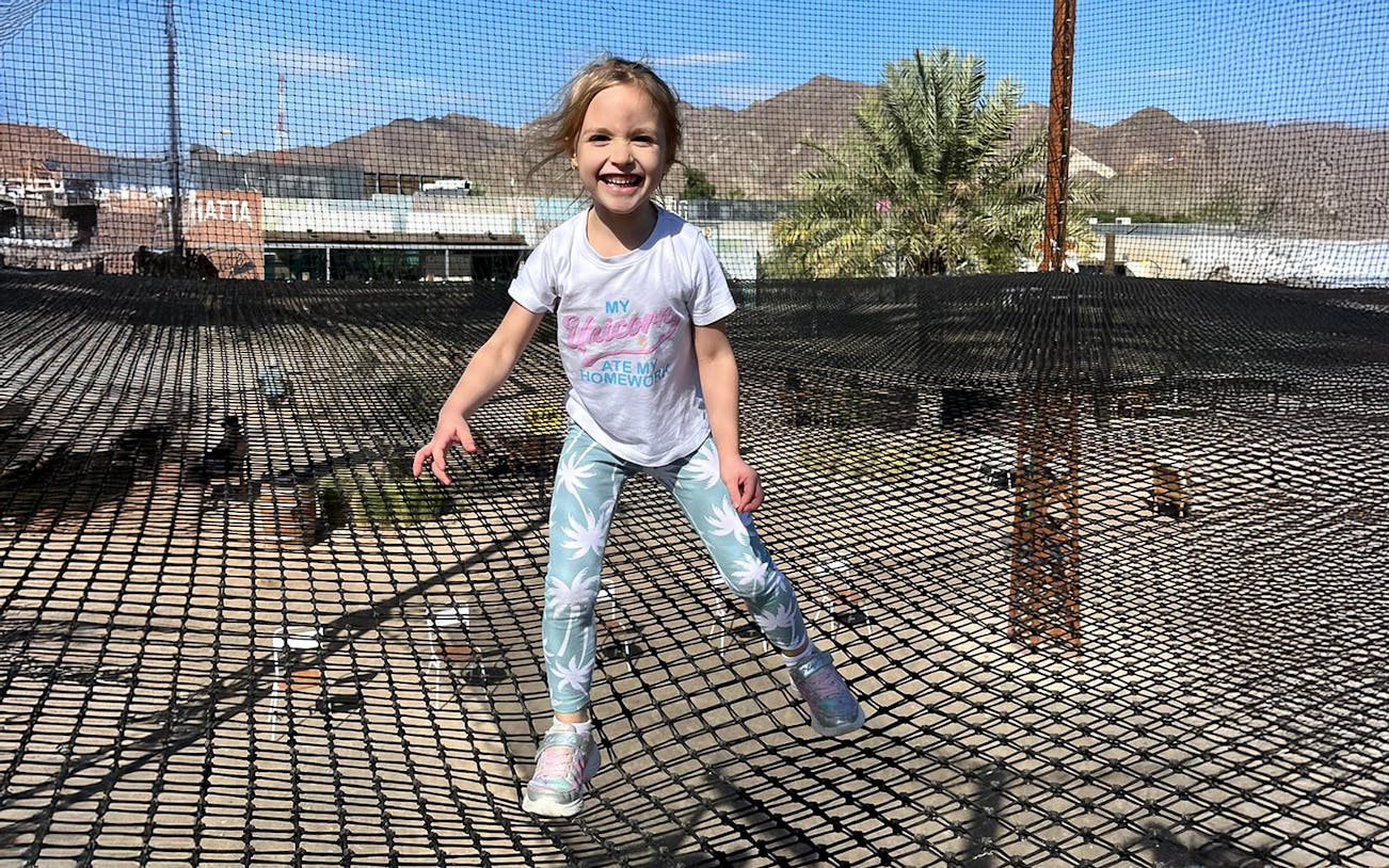 Child enjoying trampoline at Hatta Wadi Hub with mountains in the background.