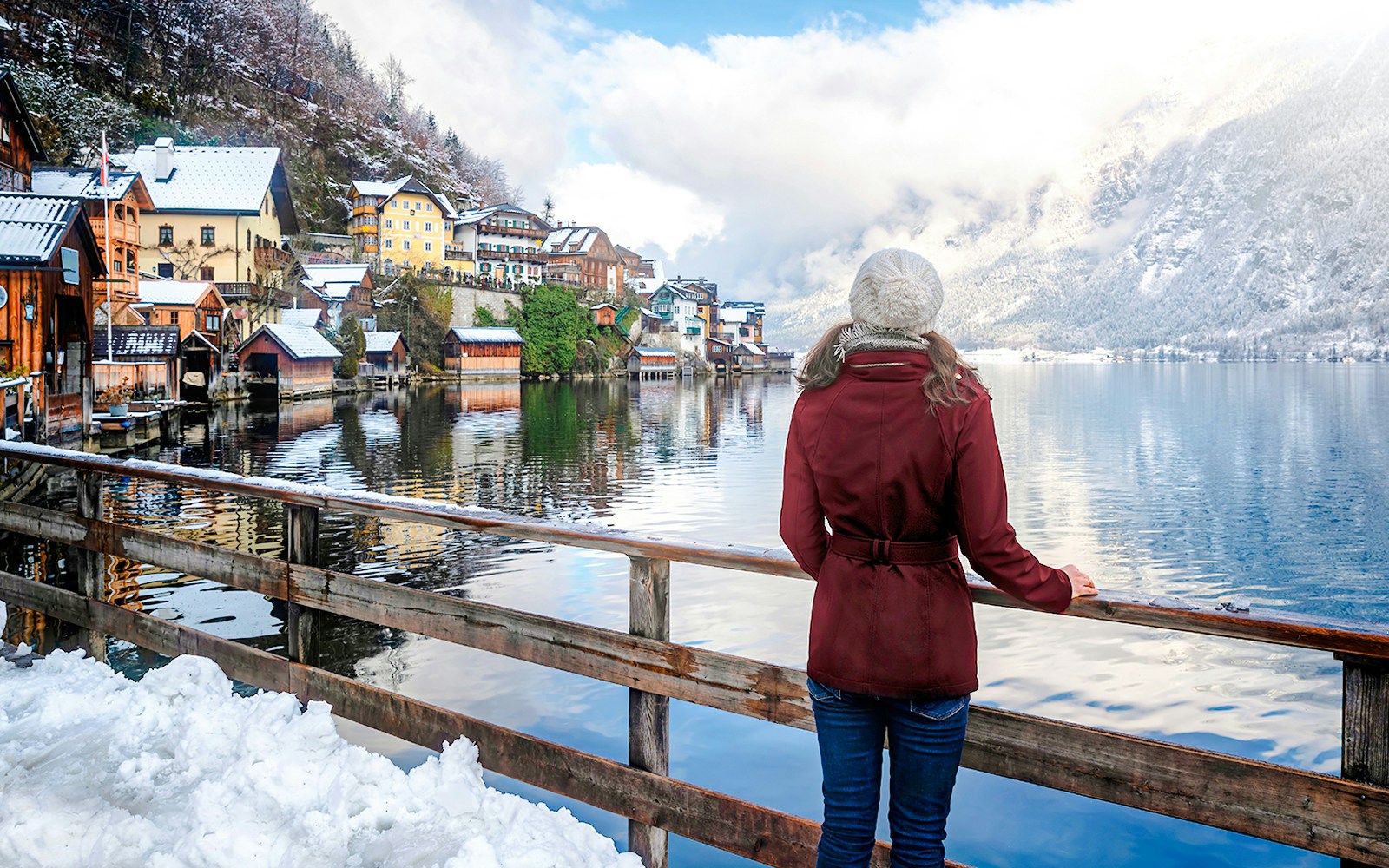 Tourist overlooking snowy village and lake in Hallstatt, Austria during winter.