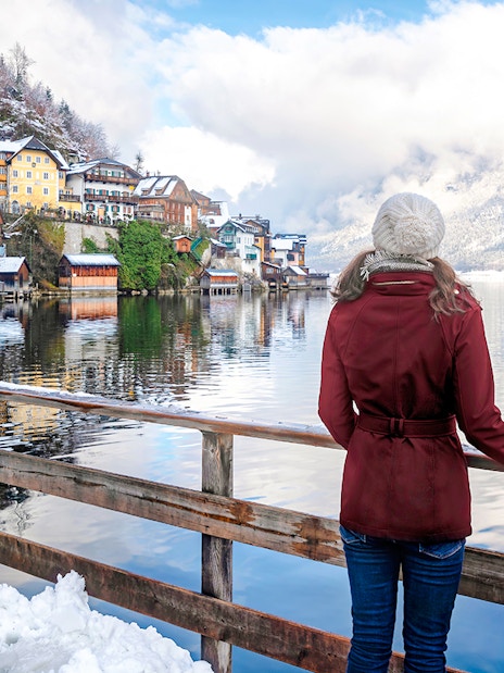 Tourist overlooking snowy village and lake in Hallstatt, Austria during winter.