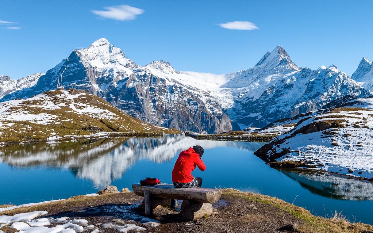 Person sitting on a bench overlooking Bachalpsee Lake with snow-capped mountains in Grindelwald First.