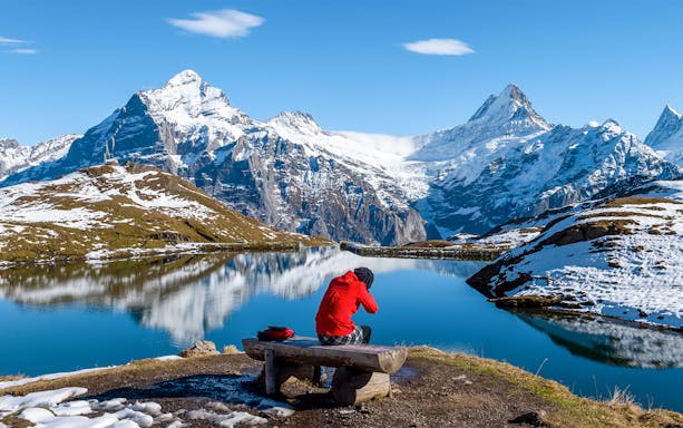 Person sitting on a bench overlooking Bachalpsee Lake with snow-capped mountains in Grindelwald First.