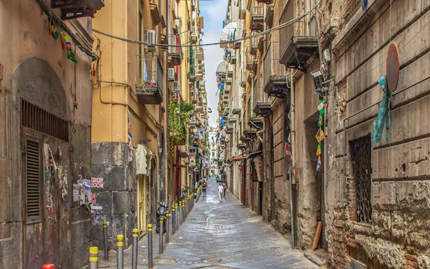 Narrow alleyway in Naples with colorful flags and historic buildings.