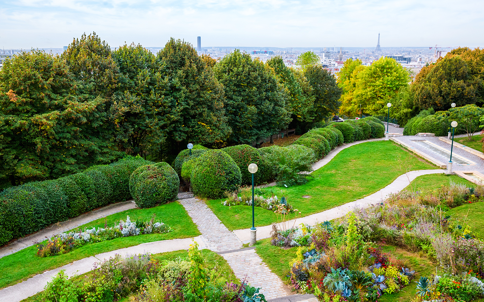 Pathways and gardens in Parc de Belleville, Paris, with city skyline in the background.