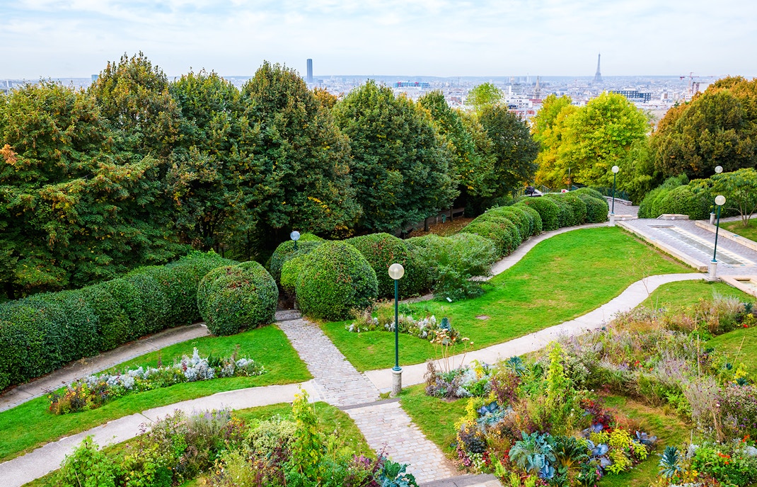 Pathways and gardens in Parc de Belleville, Paris, with city skyline in the background.