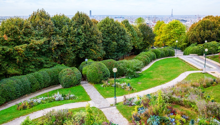 Pathways and gardens in Parc de Belleville, Paris, with city skyline in the background.