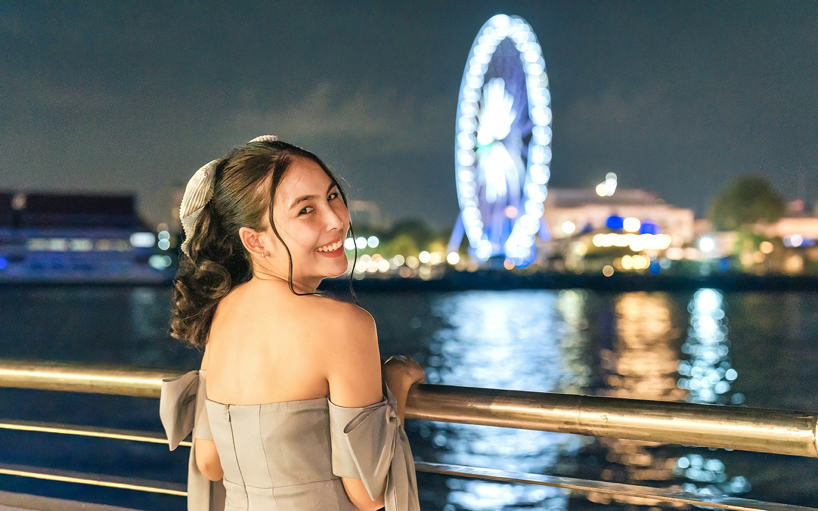 Female tourist enjoying night view on White Orchid River Cruise with Ferris wheel in background.
