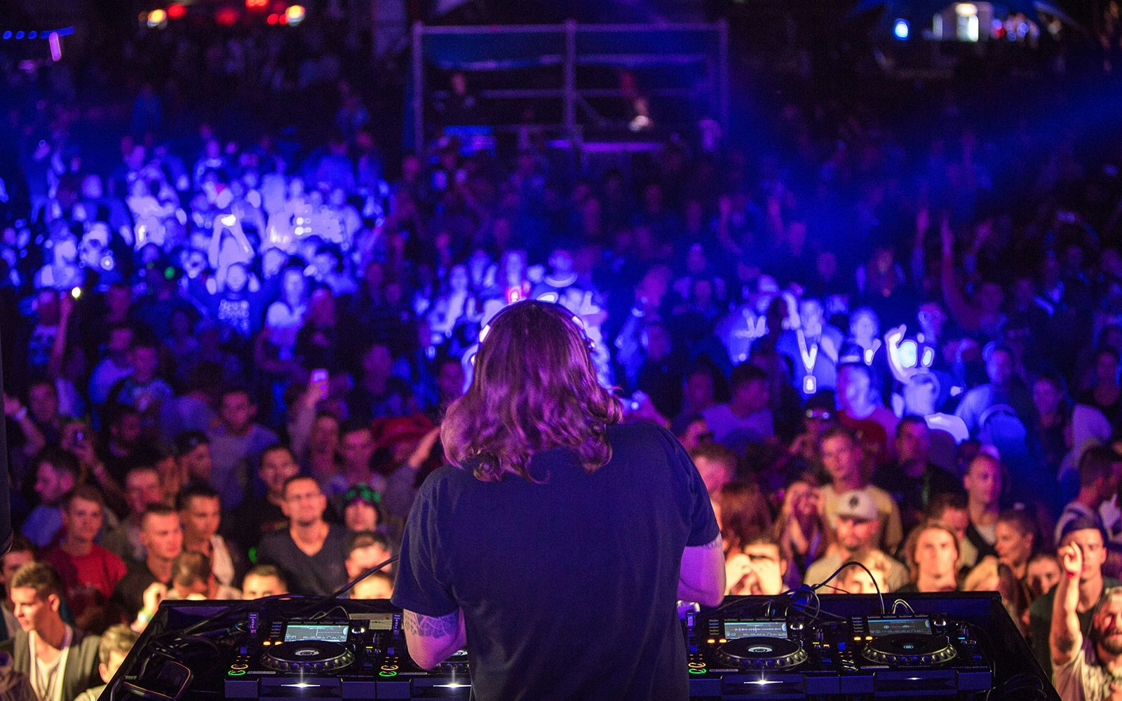 DJ performing with headphones at Ibiza nightclub party, vibrant lights in the background.