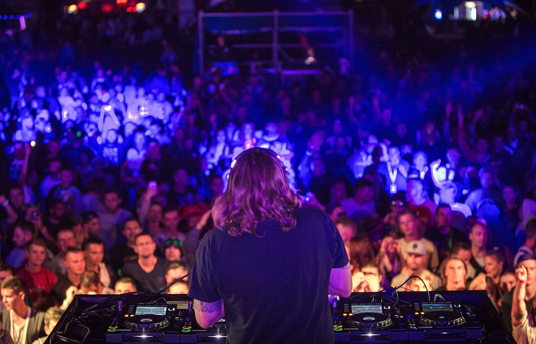DJ performing with headphones at a nightclub party, vibrant crowd in the background.