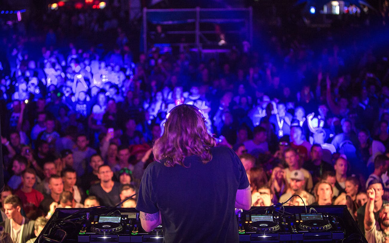 DJ performing with headphones at a nightclub party, vibrant crowd in the background.