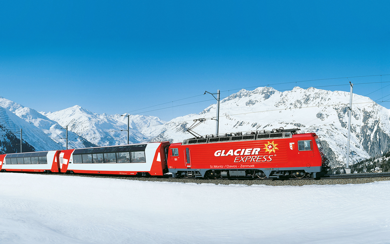 Glacier Express train traveling through snowy Swiss Alps.
