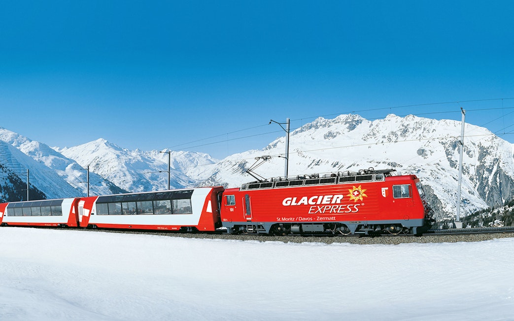 Glacier Express train traveling through snowy Swiss Alps.
