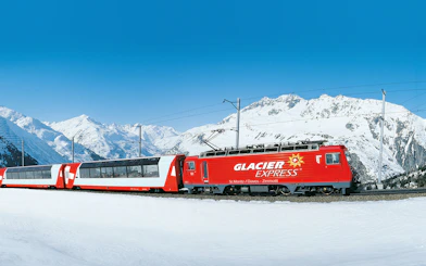Glacier Express train traveling through snowy Swiss Alps.