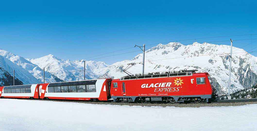 Glacier Express train traveling through snowy Swiss Alps.