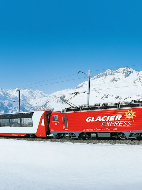 Glacier Express train traveling through snowy Swiss Alps.