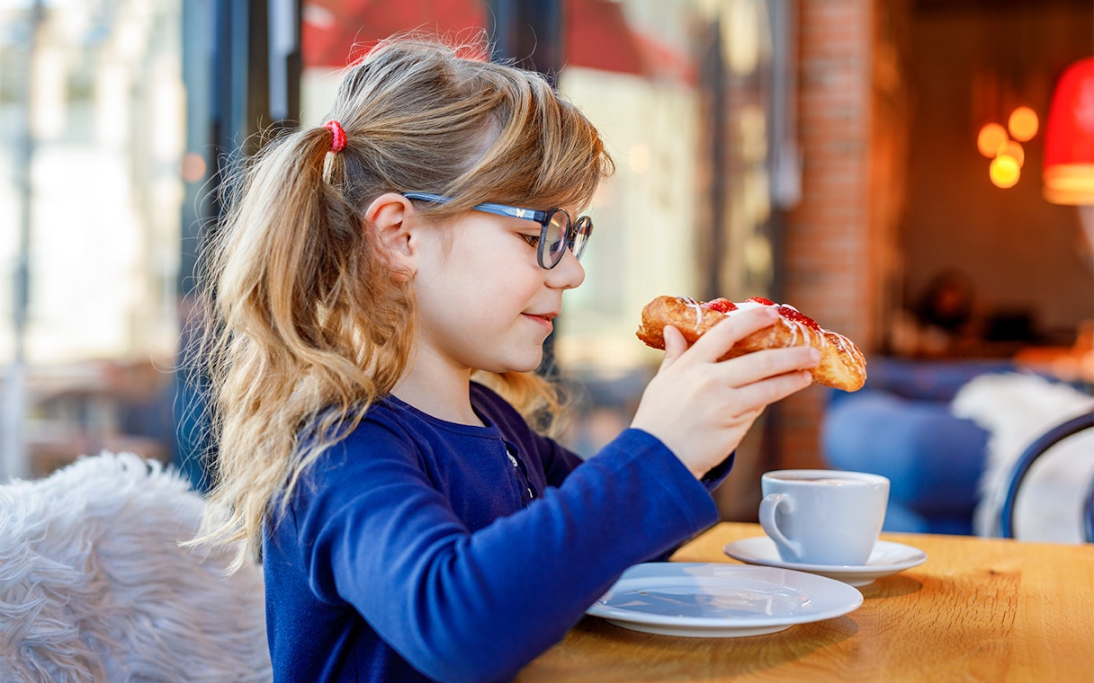 Child enjoying pastry at Brasserie Rosalie breakfast table.