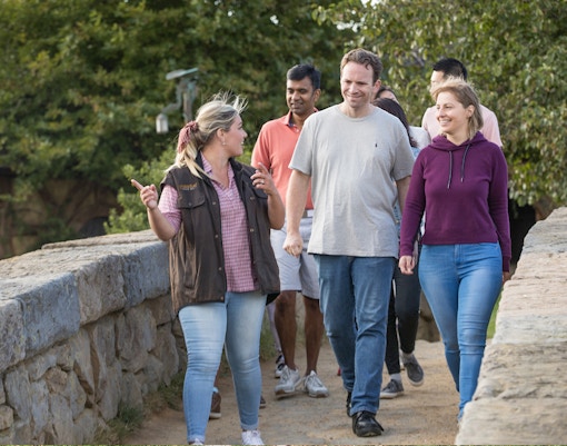 Tour guide leading group across stone bridge at Hobbiton Movie Set, surrounded by greenery.