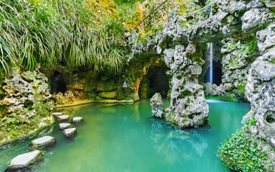 Stone pathway over turquoise water in Quinta da Regaleira garden, Sintra, Portugal.