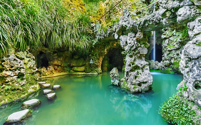 Stone pathway over turquoise water in Quinta da Regaleira garden, Sintra, Portugal.