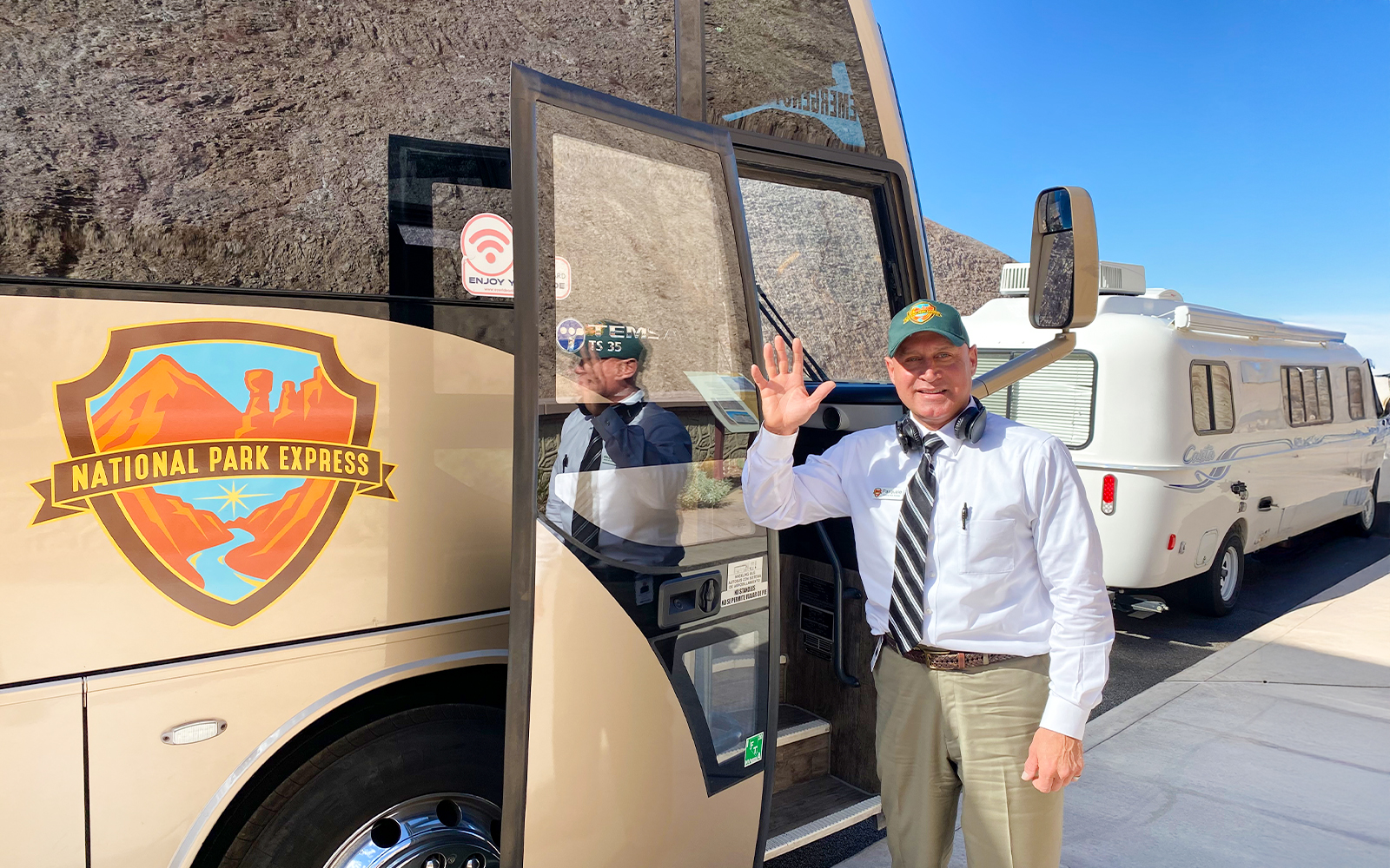 Tour bus driver waving at guests near National Park Express bus.