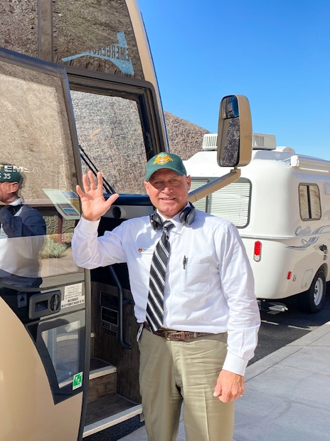 Tour bus driver waving at guests near National Park Express bus.