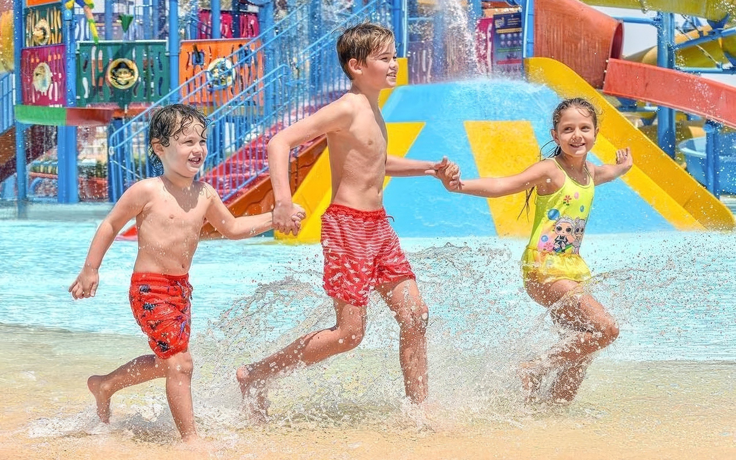 Kids running through water holding hands at Makadi Water World, Hurghada.