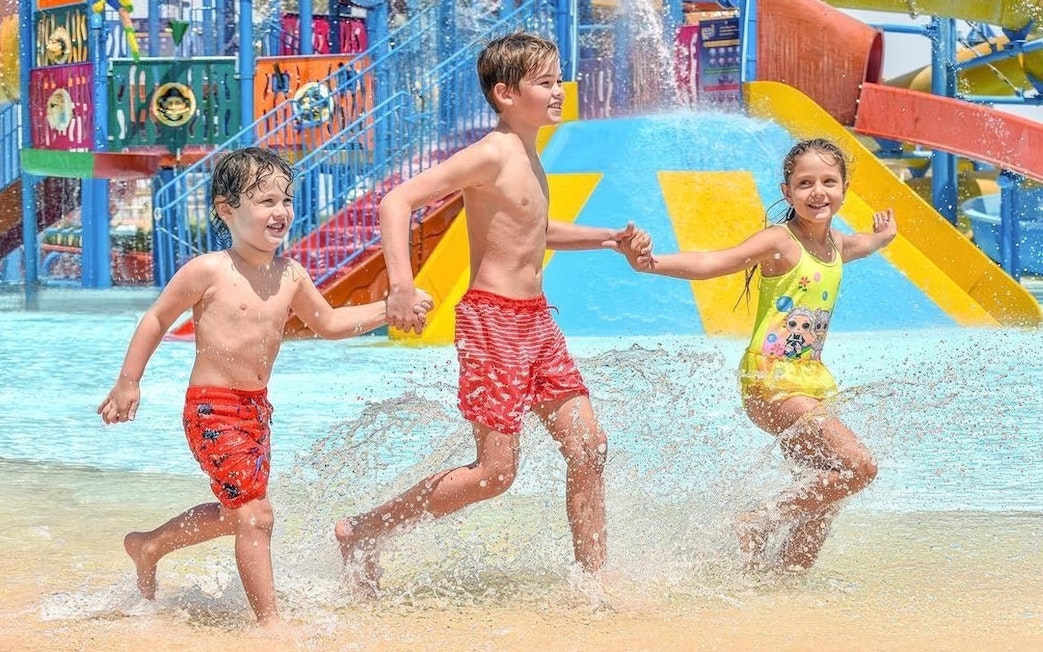 Kids running through water holding hands at Makadi Water World, Hurghada.