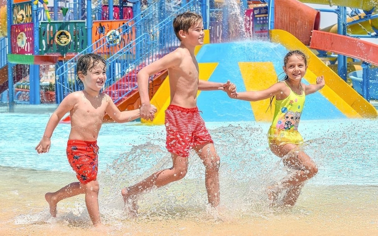 Kids running through water holding hands at Makadi Water World, Hurghada.