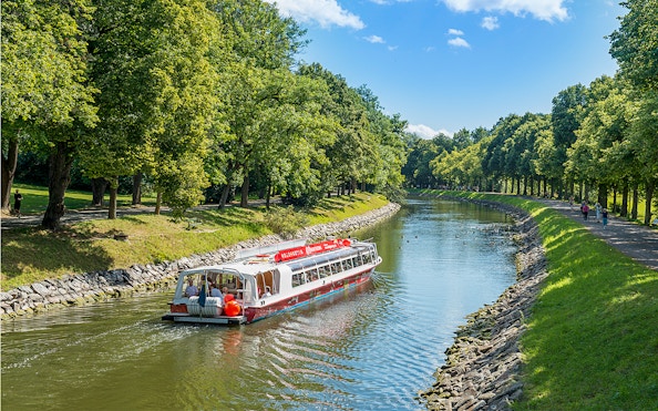 Stockholm hop-on hop-off boat cruising along a tree-lined canal.