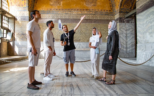 Tour group with guide inside Hagia Sophia, Istanbul, discussing historical details.