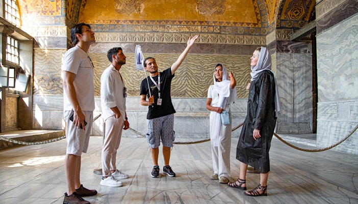 Tour group with guide inside Hagia Sophia, Istanbul, discussing historical details.