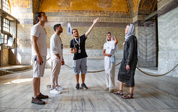 Tour group with guide inside Hagia Sophia, Istanbul, discussing historical details.