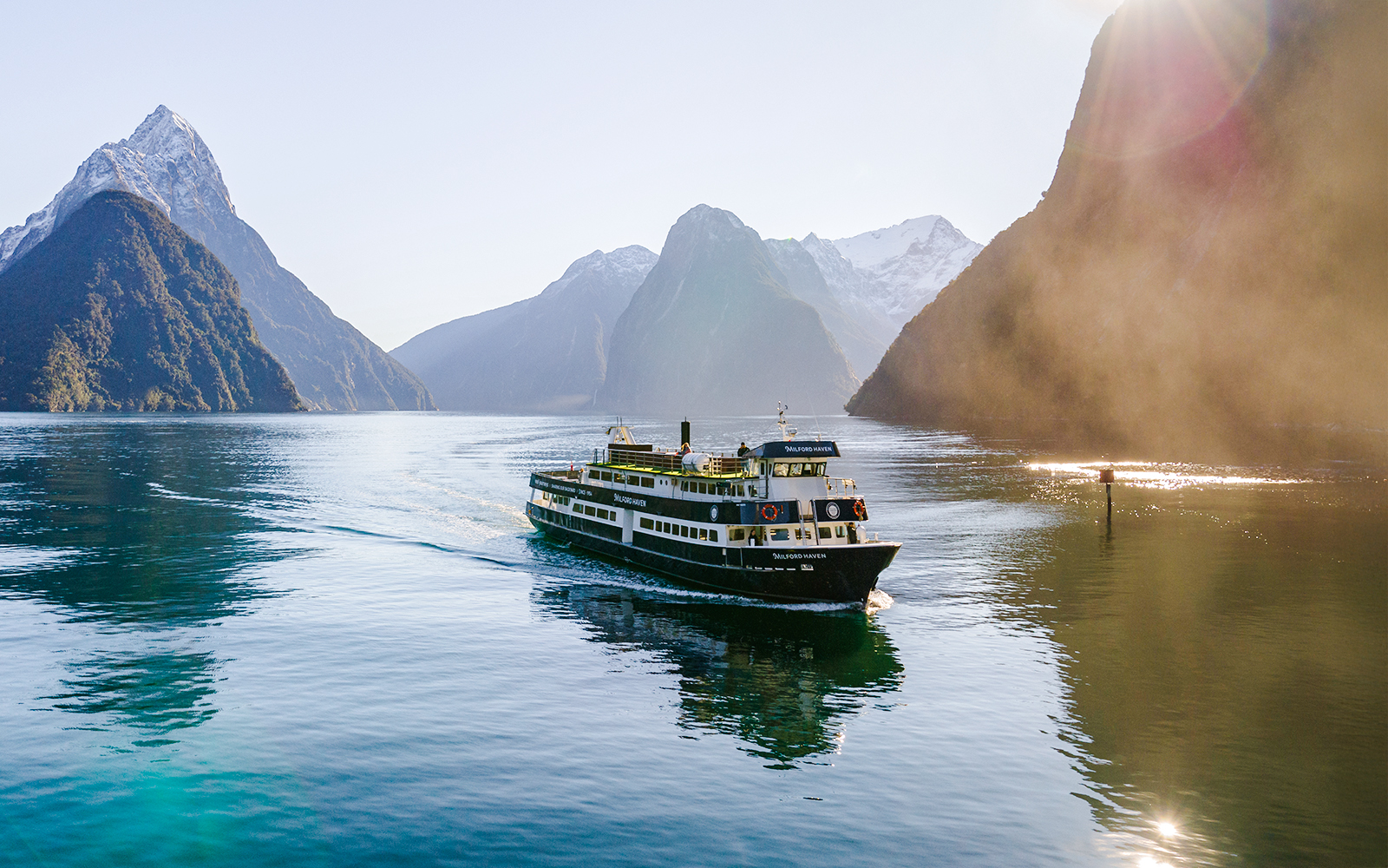 Cruise ship sailing through Milford Sound with mountain peaks in the background.