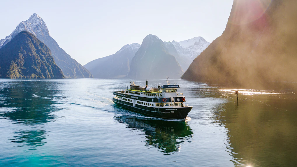 Cruise ship sailing through Milford Sound with mountain peaks in the background.