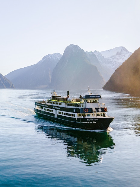 Cruise ship sailing through Milford Sound with mountain peaks in the background.