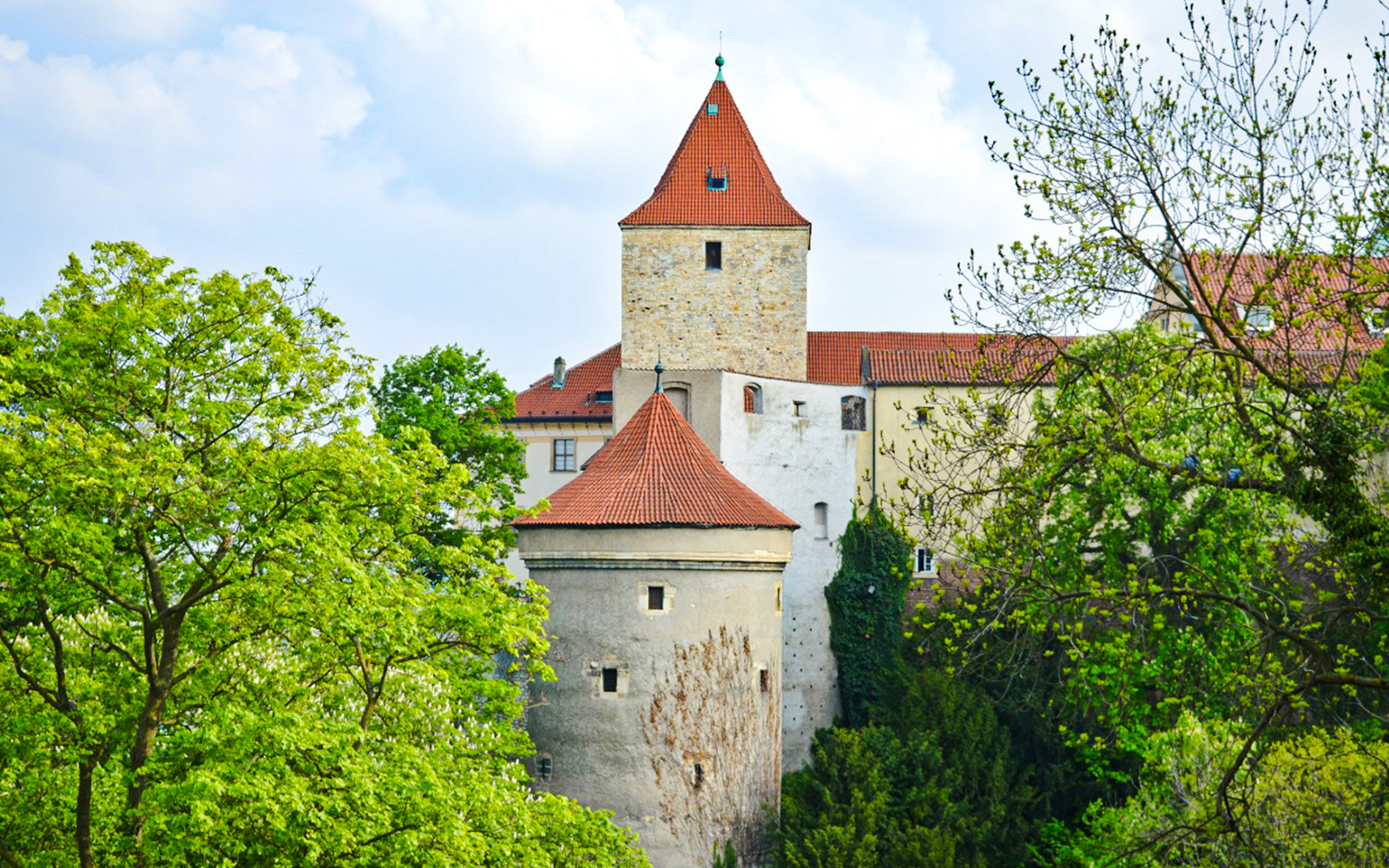 Daliborka Tower at Prague Castle surrounded by lush greenery.