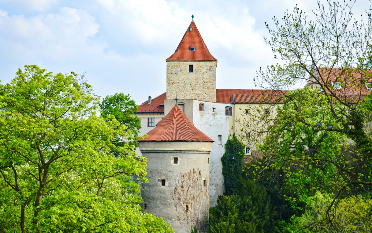 Daliborka Tower at Prague Castle surrounded by lush greenery.