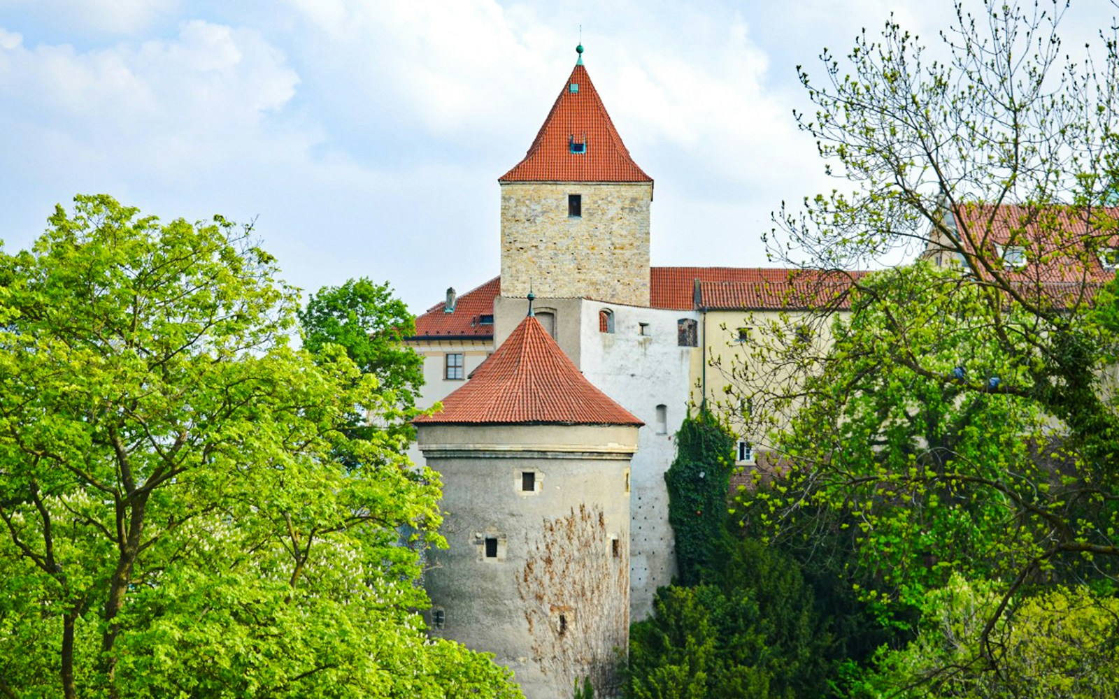 Daliborka Tower at Prague Castle surrounded by lush greenery.